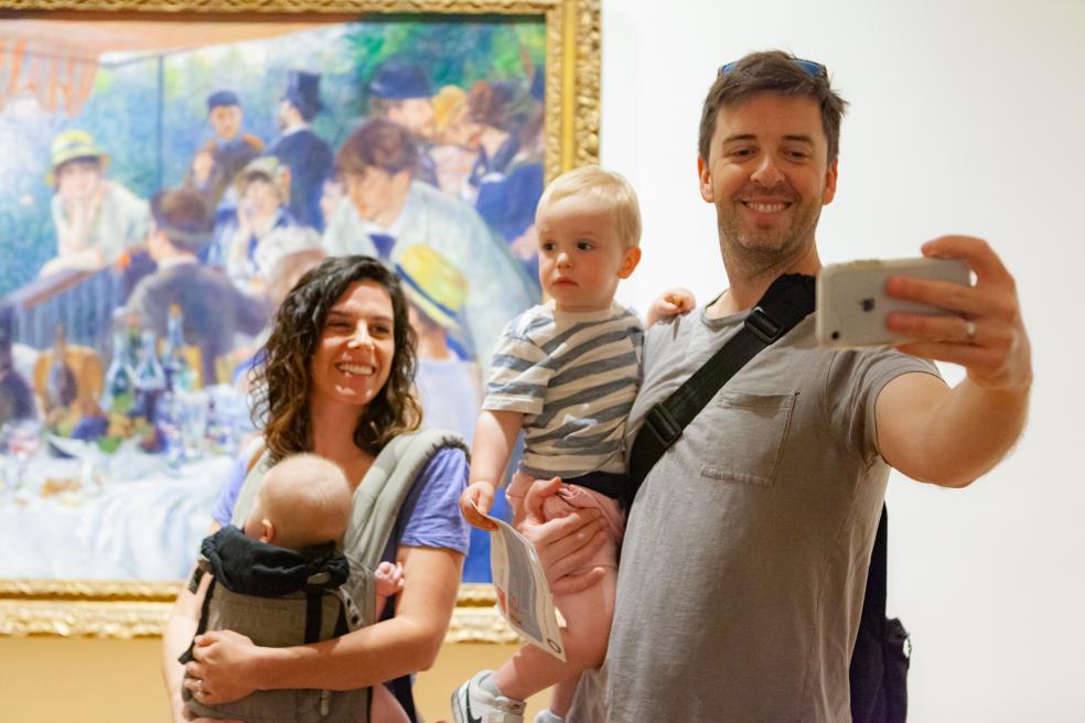 Photograph of family with two children taking a group selfie in front of Renoir's Luncheon of the Boating Party